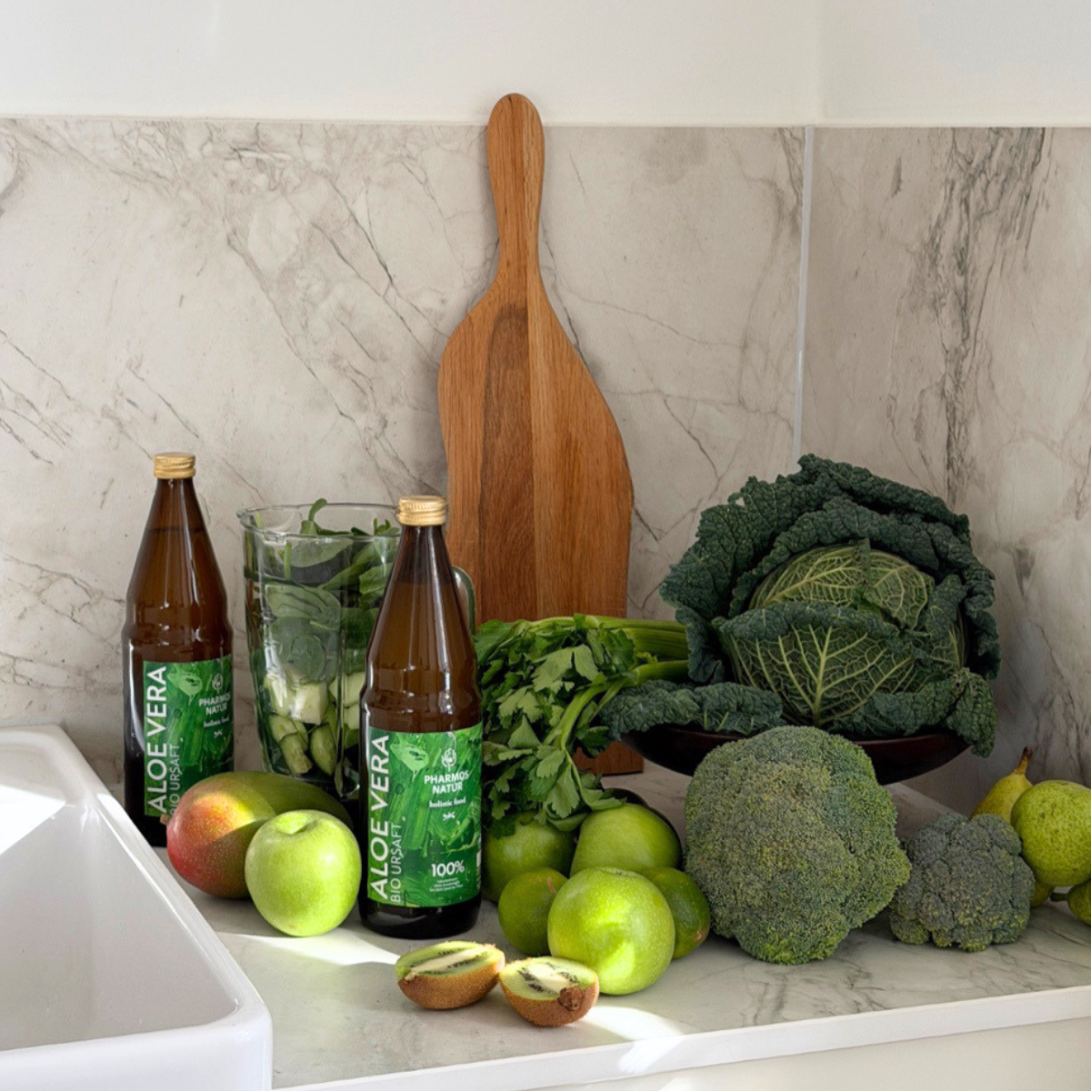 2 Flaschen Aloe Vera Bio Ursaft in Küche mit viel frischem und grünem Obst und Gemüse