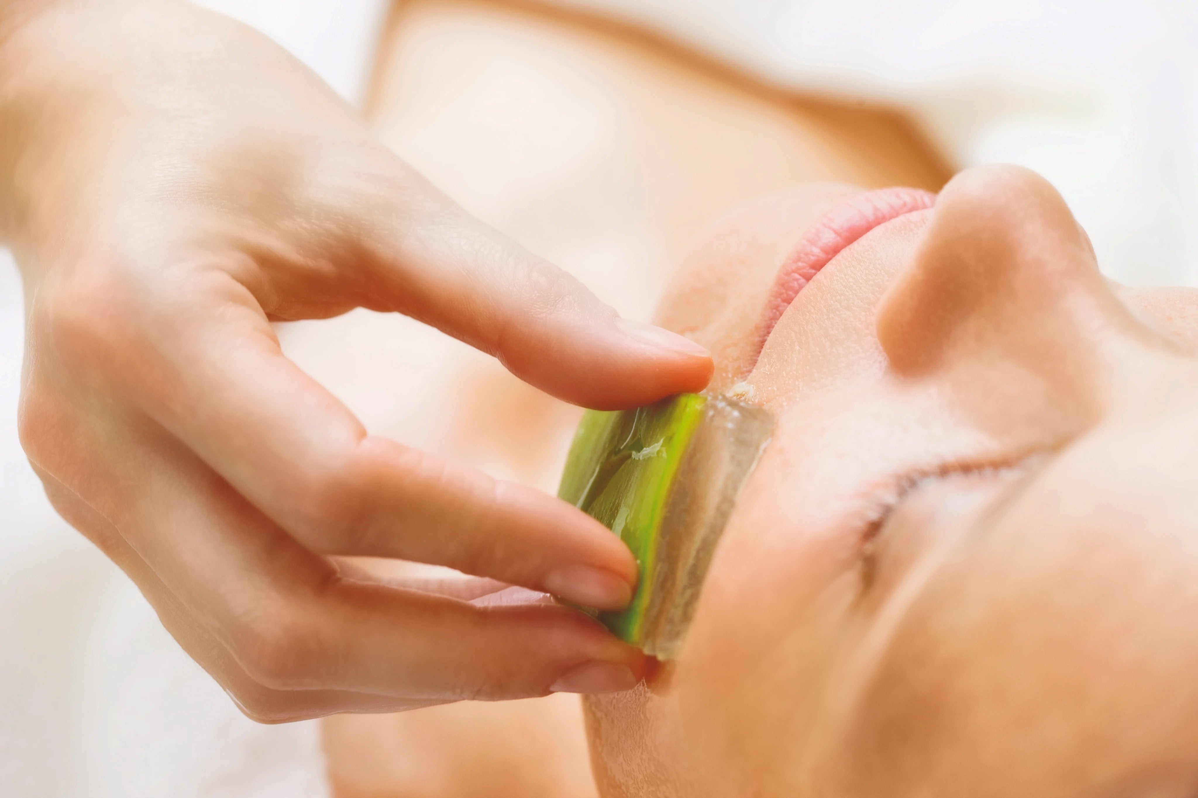 Nahaufnahme einer Frau bei der Behandlung mit einem Stück Aloe Vera 