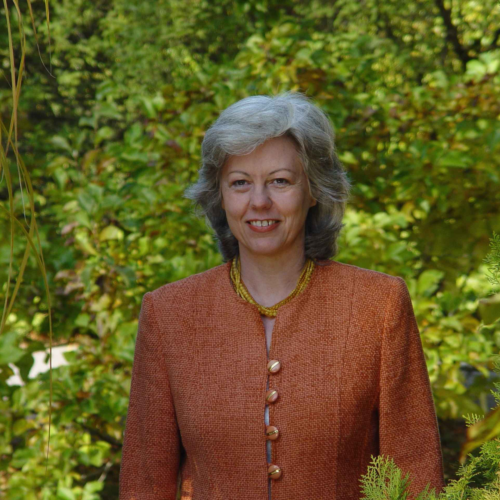 Die Gründerin Margot Esser Portrait in orangenem Sakko mit grünem Hintergrund
