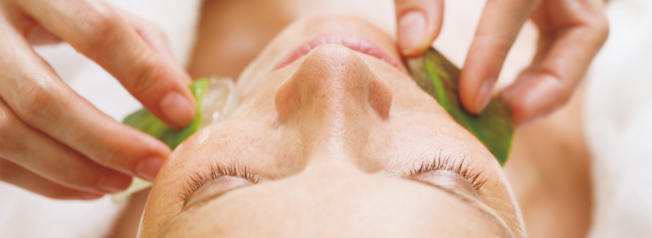 Behandlung Gesicht einer Frau von oben, während ihr auf die Backen jeweils eine Aloe Vera Scheibe eingerieben wird